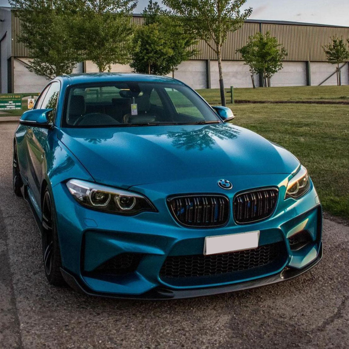 Gloss black carbon fiber front lip for BMW F87 M2 (2016-2018) by Palenon Performance, shown on the front left of the car.