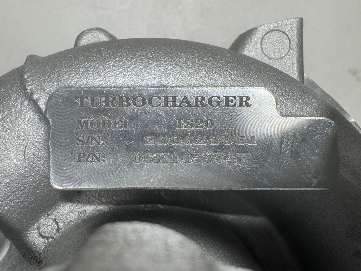 Close-up of a metallic turbocharger housing with an embossed metal nameplate reading TURBOCHARGER, model 06K145874T, and serial details.