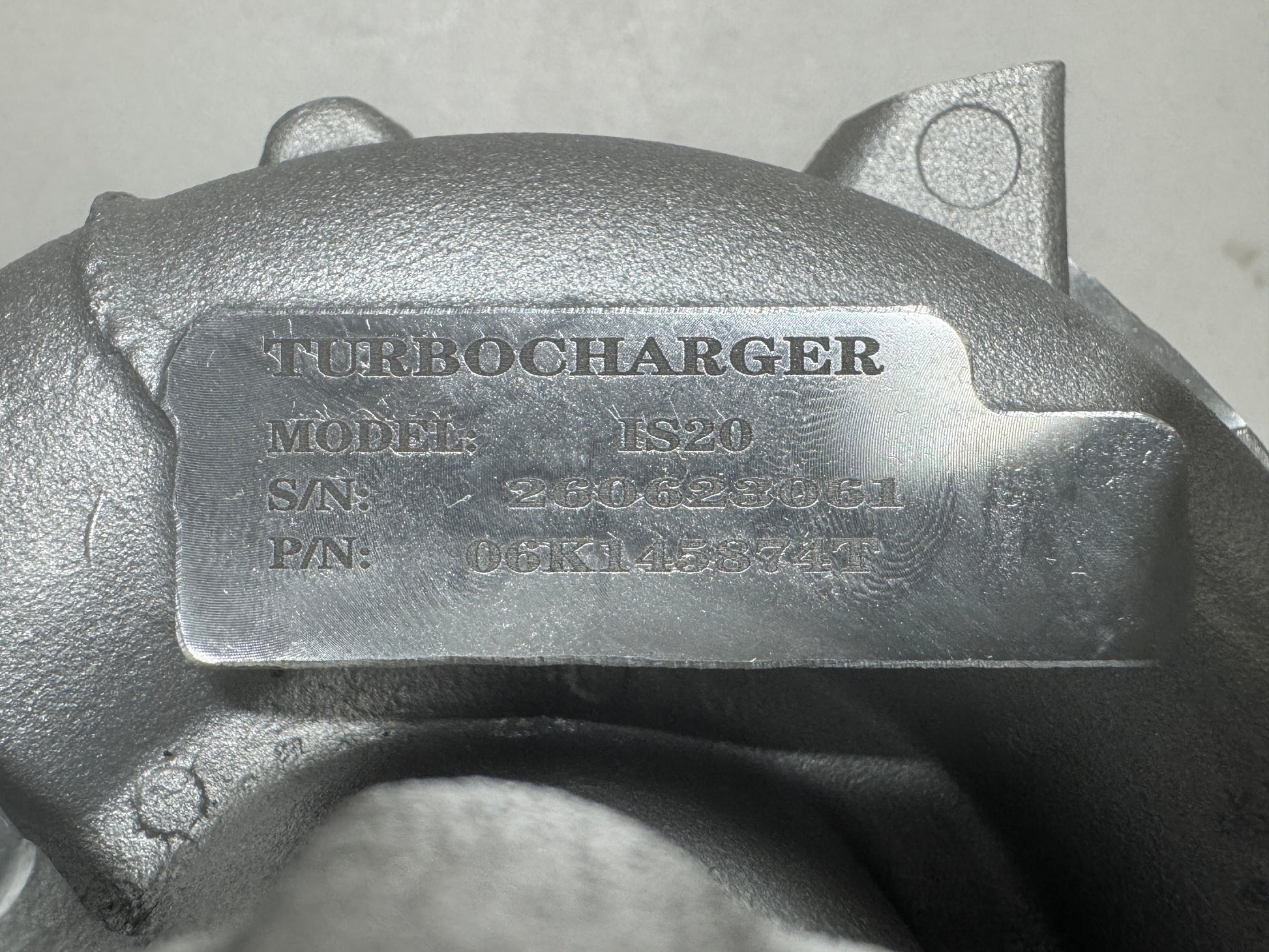 Close-up of a metallic turbocharger housing with an embossed metal nameplate reading TURBOCHARGER, model 06K145874T, and serial details.