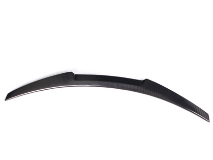 BMW F82 M4 V Style trunk spoiler in carbon fiber, rear view showing sleek aerodynamic design and textured carbon surface.